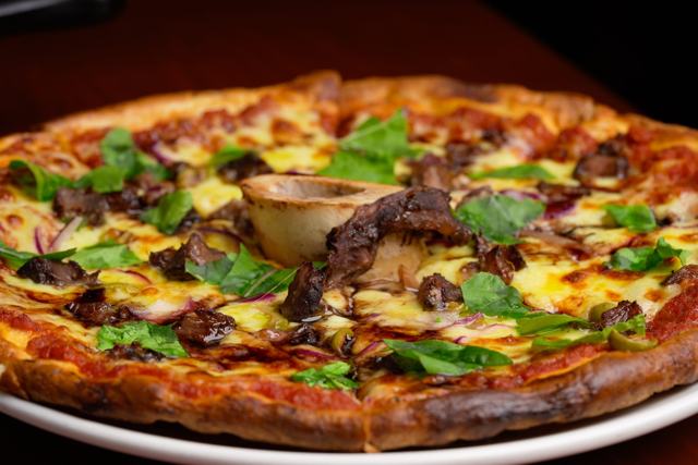 Pizza con queso gratinado, carne oscura en trozos, cebolla morada y hojas de albahaca.