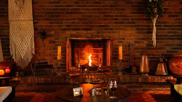 Chimenea de ladrillo encendida, con velas, un macramé colgado y objetos de cobre.