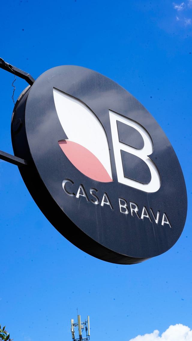 Rótulo circular de Casa Brava, oscuro con la letra B y dos hojas, contra un cielo azul.