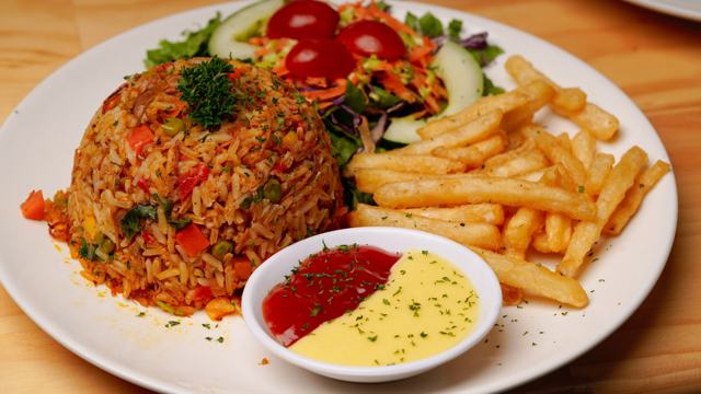 Plato de arroz salteado con verduras moldeado en cúpula, papas fritas, ensalada con tomate cherry y salsas de tomate y mostaza.
