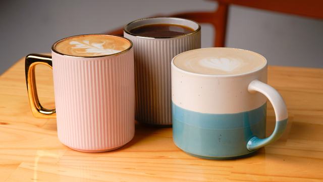 Tres tazas de cerámica con café: una rosada con asa dorada, una gris y una blanca con celeste.