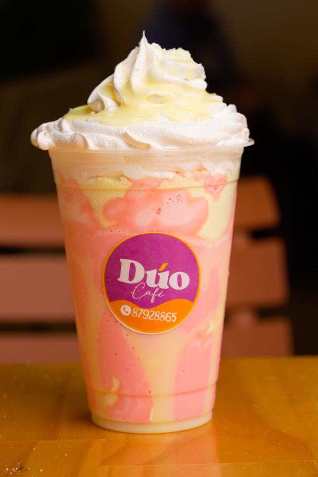 Vaso plástico con un batido rosado y amarillo, crema batida y la etiqueta de Dúo Café.