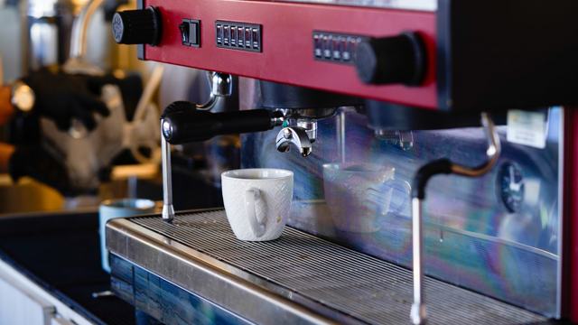 Máquina de espresso roja con una taza blanca bajo el portafiltro.