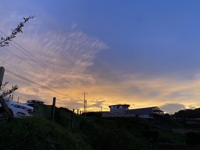 Cielo de atardecer con nubes anaranjadas y moradas sobre siluetas de casas y lomas.