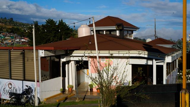 Edificio de un piso con techo rojo a cuatro aguas y paredes blancas, visto desde la calle.