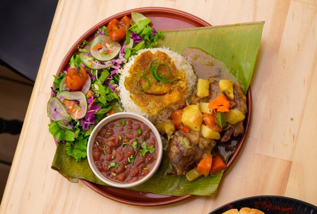 Plato sobre hoja de plátano con arroz, frijoles, ensalada, carne en salsa con papa y zanahoria.