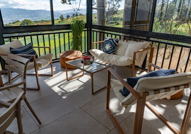 Terraza con sillones de madera y cojines alrededor de una mesa baja, con baranda y vista al valle.