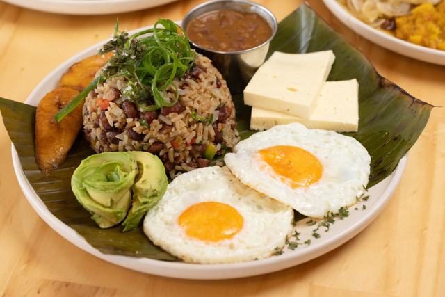 Gallo pinto con dos huevos fritos, queso blanco, plátano maduro, aguacate y frijoles molidos, sobre hoja de plátano.