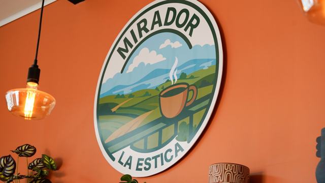 Rótulo circular de Mirador La Estica sobre una pared terracota, con una lámpara colgante.